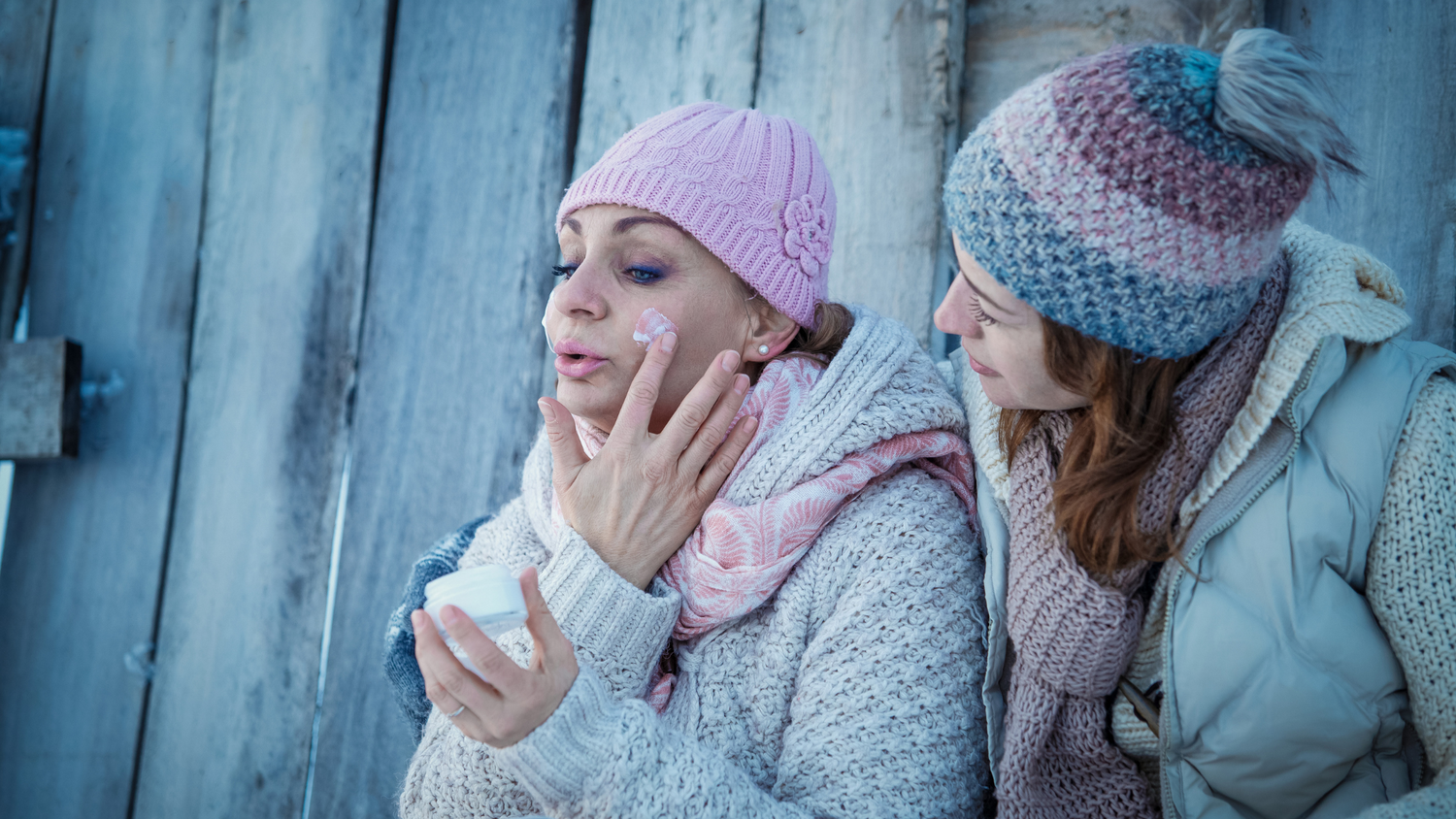 Two women applying moisturizer in winter gear
