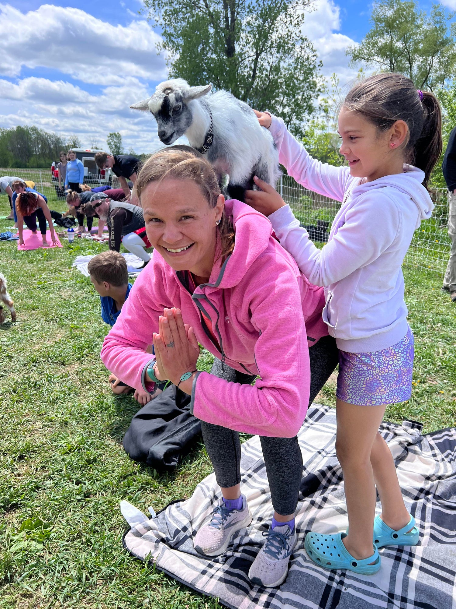 Lady and child at goat yoga. Baby goat on participants back. 